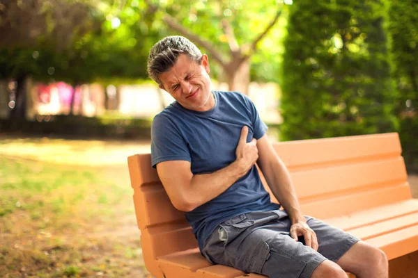 心の痛みを屋外で男 公園のベンチに座って胸の痛みを感じる男性 医療の概念 — ストック写真