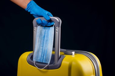 Tıbbi maskeli bir bavul. Bagajı tutan tıbbi eldivenleri teslim edin. Seyahat ve koronavirüs konsepti. Stüdyo çekimi