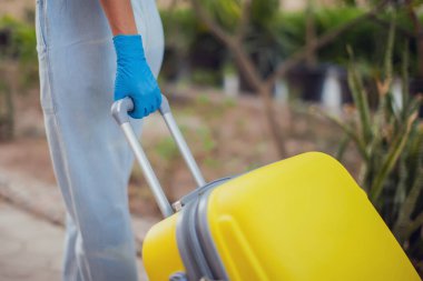 Seyahat ve koronavirüs konsepti. Tıbbi eldivenli bir kadın sokakta bavul tutuyor.