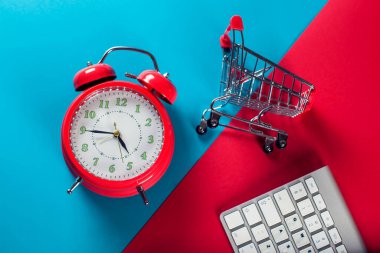Kırmızı çalar saat, alışveriş arabası ve arka planda çift renkli klavye. Çevrimiçi alışveriş ve satış kavramı