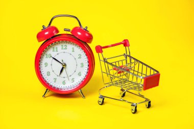 Kırmızı alarmlı saat, arka planda küçük bir alışveriş arabası. Alışveriş konsepti