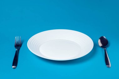 Mavi arka planda beyaz tabak, çatal ve kaşık.