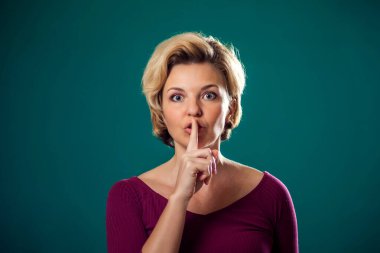 Kısa sarı saçlı, sessiz jest yapan bir kadın. İnsanlar ve duygular