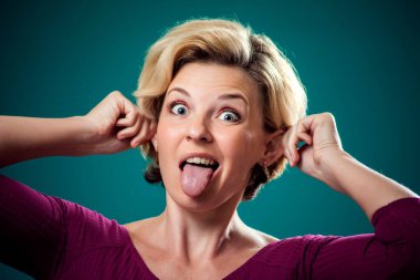 Kısa sarı saçlı komik görünüşlü bir kadın komik bir surat yapıyor. Dilini ve kulaklarını gösteriyor. İnsanlar, yaşam tarzı ve duygu kavramı