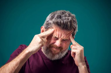 Kırmızı tişörtlü sakallı bir adamın portresi ya çok düşünüyor ya da başı ağrıyor. İnsanlar, duygular ve sağlık kavramı