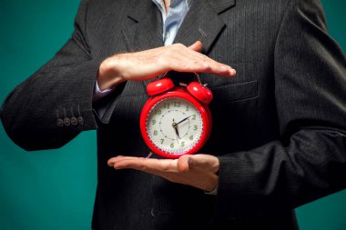 Sakallı iş adamı elinde kırmızı alarm saati tutuyor. Zaman yönetimi kavramı