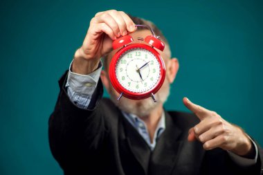 Sakallı iş adamı elinde kırmızı çalar saat tutuyor ve parmağıyla işaret ediyor. Zaman yönetimi kavramı