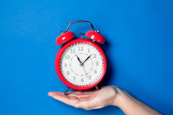 Рука человека, держащего красный будильник на цветном фоне