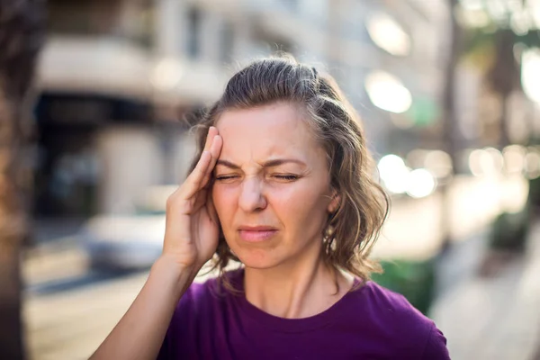 Female feeling headache on the street. Stressed woman outside