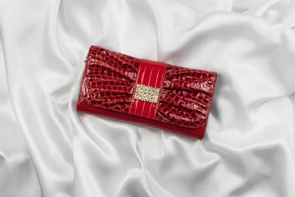 Red lacquer bag inlaid with diamonds lying on a white silk Rechtenvrije Stockafbeeldingen