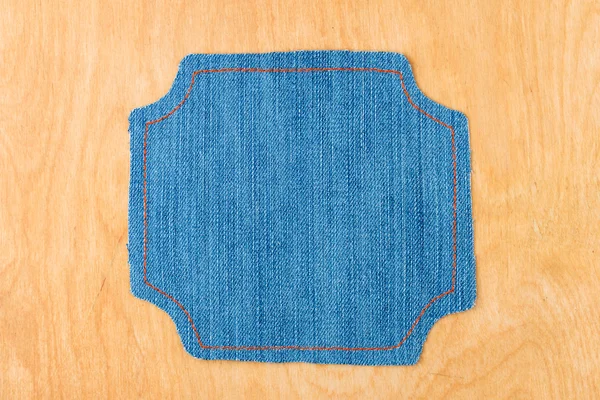 Figured frame made of denim is lying on a light wood surface — Stock Photo, Image