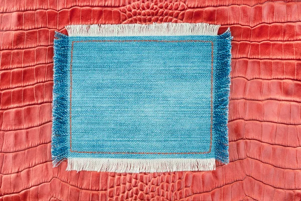 Frame made of denim with a fringe is on the red crocodile skin — Stock Photo, Image