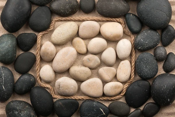 Rám z lana, ležící na písku mezi bílými a černými kameny — Stock fotografie