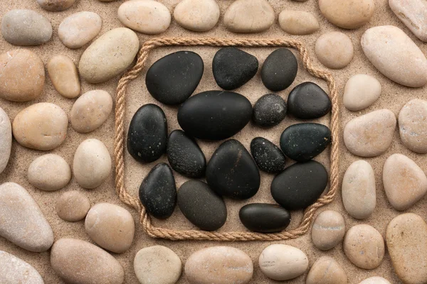 Frame made of rope lying on the sand among the black and white stones — Stock Photo, Image