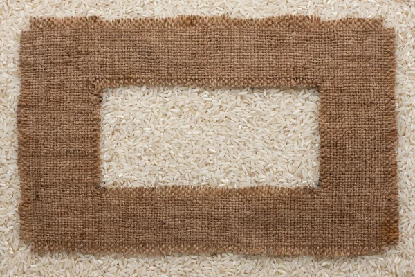 Frame made of rough burlap lies on rice grains — Stock Photo, Image