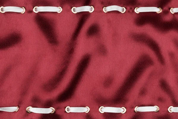 White satin ribbon inserted in the gold rings on red silk — Stock Photo, Image