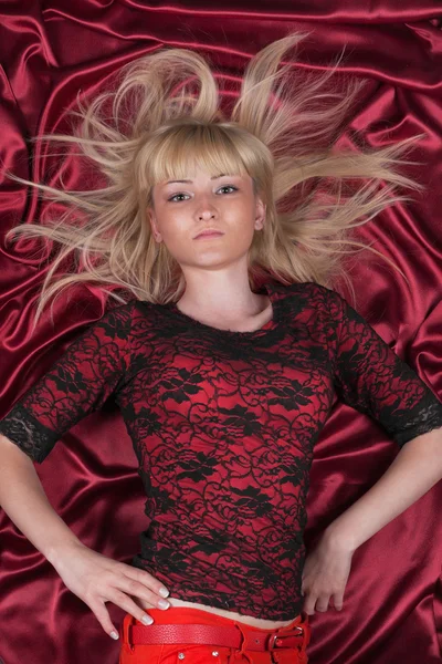 Blonde Hair. Beautiful girl lying on a red cloth — Stock Photo, Image