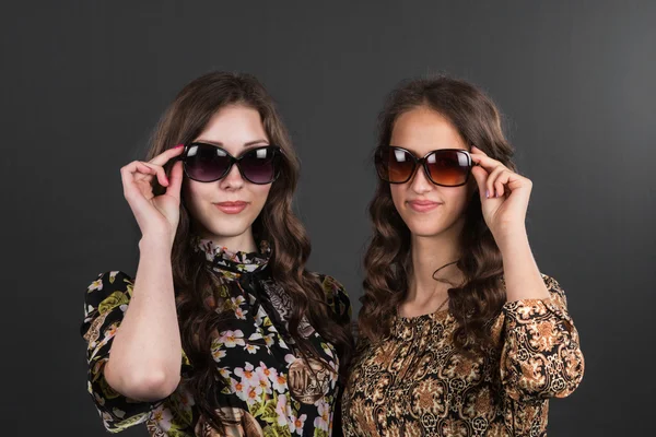 Dwie piękne dziewczyny szczęśliwy w okulary na szarym tle. — Zdjęcie stockowe