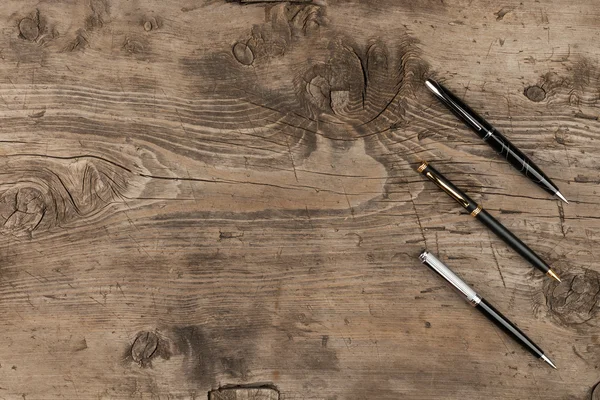 Black, gold and silver pens on a wooden texture — Stock Photo, Image