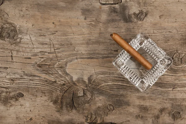 Glass ashtray with cigar stands on a wooden surface — Stock Photo, Image