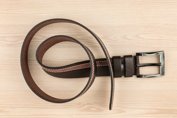 Brown leather belt with buckle lying on a wooden surface — Stock Photo, Image