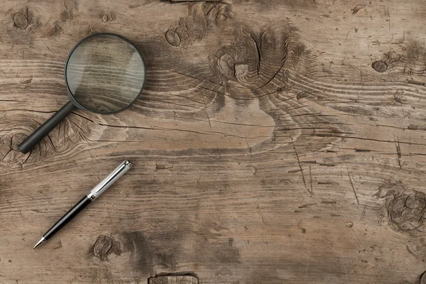 Magnifying glass and a pen lying on old wooden texture — Stock Photo, Image
