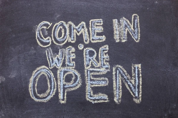 Come in we\'re open. Chalk lettering on blackboard. Multi colored inscription on a chalkboard