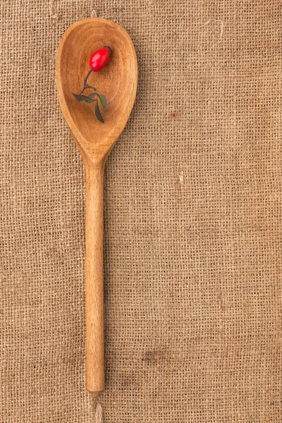 Wooden spoon with rosehip lying on sackcloth — Stock Photo, Image