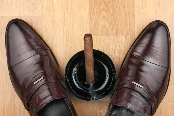 Zapatos clásicos para hombre, cenicero y cigarro humeante en el flo de madera — Foto de Stock