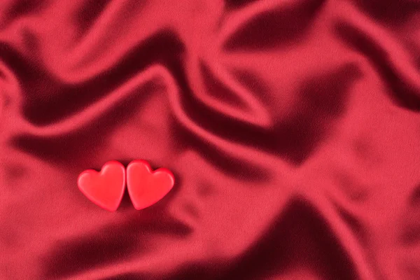 Концепция двух влюбленных сердец лежащих на красном атласе — стоковое фото