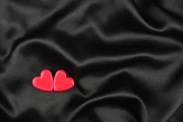 The concept of two lovers hearts lying on the black satin — Stock Photo, Image