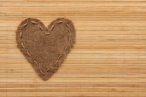 The symbolic heart of burlap lies on a bamboo mat — Stock Photo, Image
