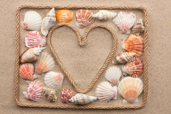 Corazón simbólico hecho de cuerda y conchas marinas que yacen sobre la arena — Foto de Stock