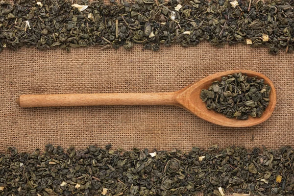 Holzlöffel mit grünem Tee liegt auf Sacktuch — Stockfoto