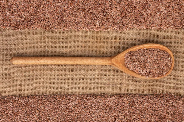 Colher de madeira com sementes de linho está em pano de saco — Fotografia de Stock