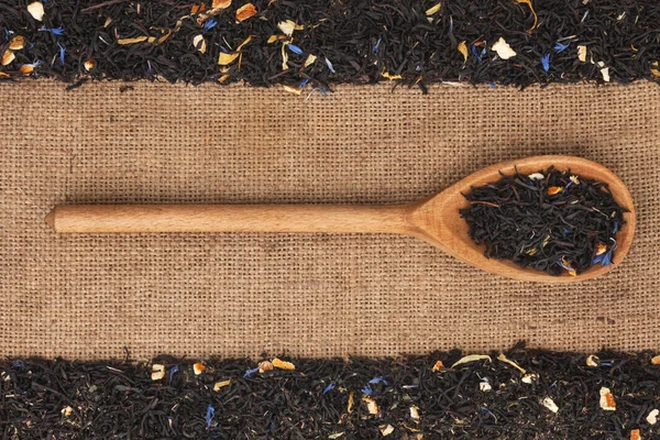 Träsked med svart te ligger på säckväv — Stockfoto