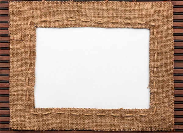 Frame made of burlap with white background lying on a bamboo mat