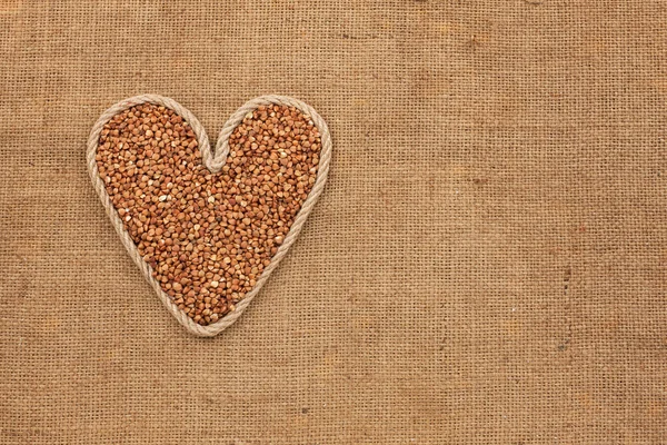 Cuore realizzato in corda con grani di grano saraceno sdraiato su sacco — Foto Stock