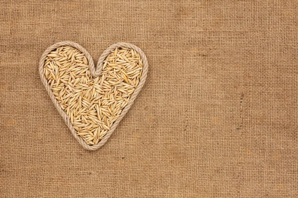 Corazón hecho de cuerda con granos de avena acostados en saco — Foto de Stock