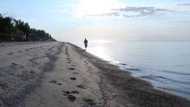 Άνθρωπος τζόκινγκ στην παραλία με την Ανατολή, ηλιοβασίλεμα. — Αρχείο Βίντεο
