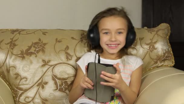 Chica sentada con una tableta y escuchando música en los auriculares . — Vídeos de Stock