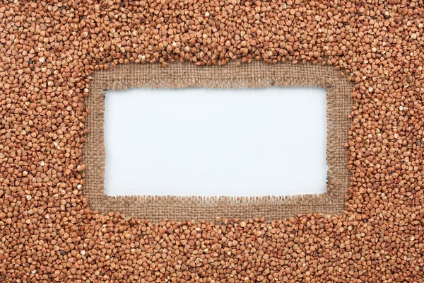 Frame made of burlap and buckwheat grains lies on white background — Stock Photo, Image