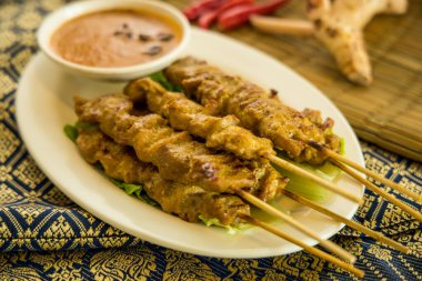 Fıstık sosu ve marulla servis edilen, acı biber ve baharatla süslenmiş tavuk şişleri..