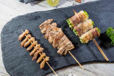 Izgara tavuk kalbi, domuz eti ve limon ve tuzlu süslemeli pastırmaya sarılmış sebze şişleri..