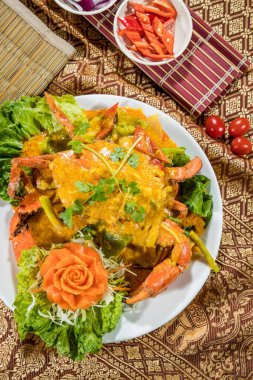 Zengin sarı köri soslu, sebzeli ve oyulmuş havuç soslu Tayland usulü yengeç, kültürel sunumla birlikte beyaz bir tabakta servis ediliyor..
