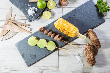 Izgara mısır, et parçaları ve yeşil dilimler kireç, tuz ve sade aksesuarlı tahta üzerinde..