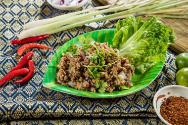Marulla servis edilen ve geleneksel malzemelerle çevrelenmiş kıyma, ot ve baharatlı Tayland larb salatası..