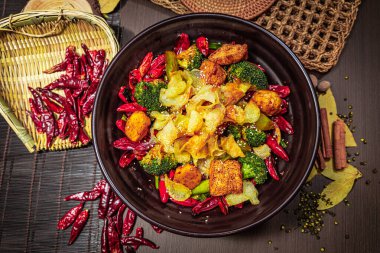 Kızarmış tofu, patates, brokoli ve susam tohumları ve sade aksesuarlarla dolu siyah bir kasede kırmızı biber..