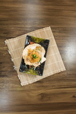 Kabuklu ızgara deniz tarağı. Üstünde ekmek kırıntısı ve yeşil soğan var. Bambu hasırının üzerinde..