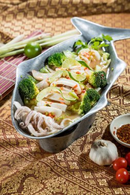 Balık şekilli kalamar halkaları, karides, brokoli, ıhlamur suyu ve biber çorbası, Tayland bitkileri ve desenli kumaş üzerindeki baharatlarla çevrili..